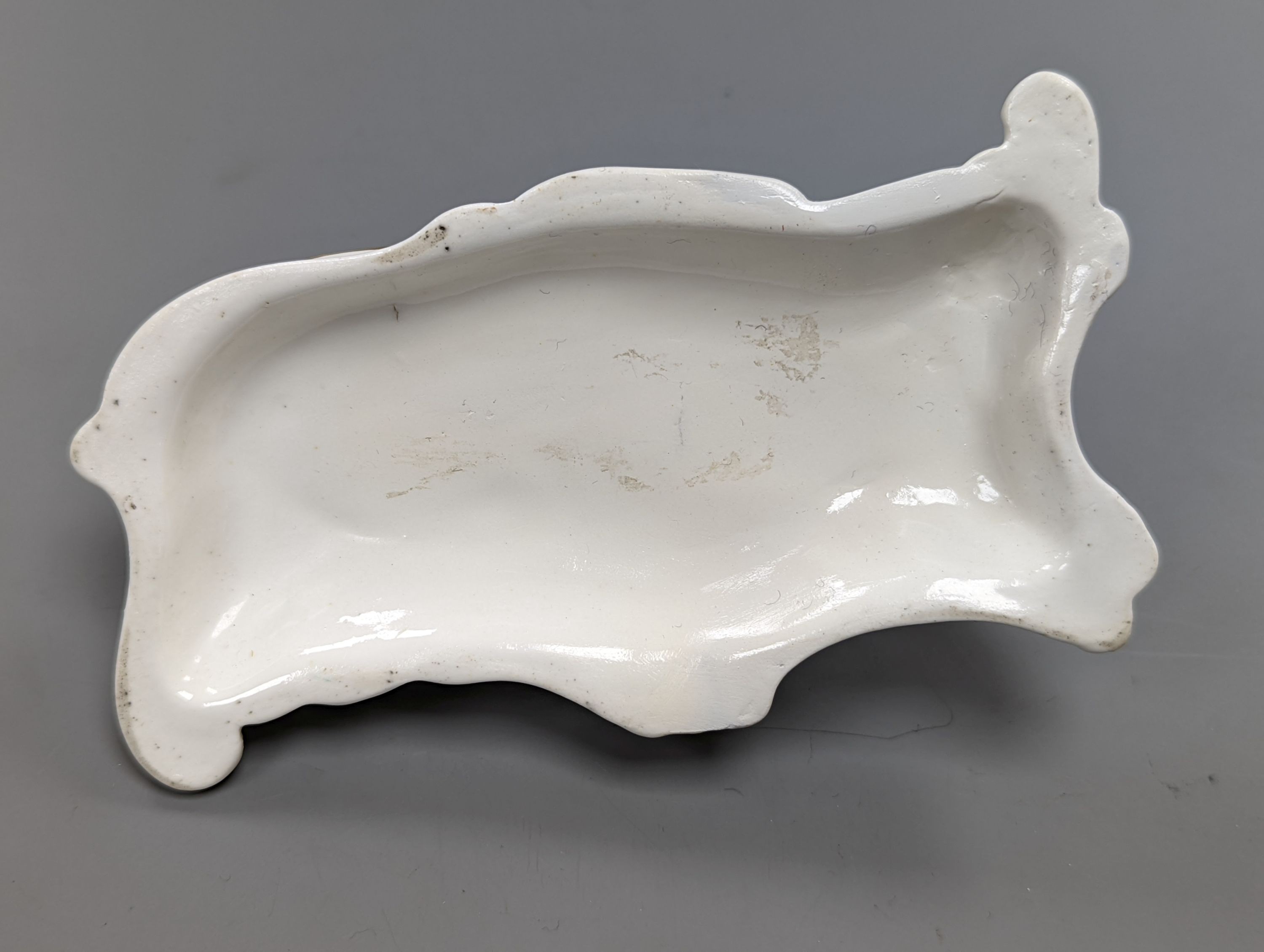 A rare Staffordshire porcelain figure of a recumbent tabby cat, c.1830-50, on a scroll work base, 11.5 cm long